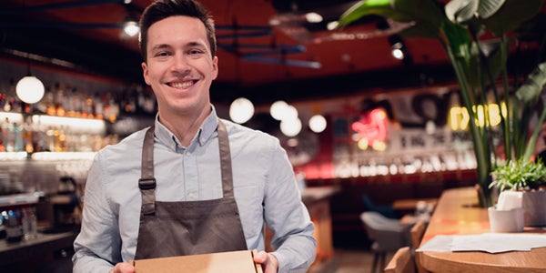 Man smiling, holding a box, in a restaurant